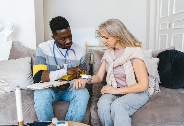 Man and woman sitting on couch doing blood pressure check.
