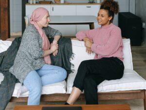 Two women talk on a couch, one is wearing a head covering.